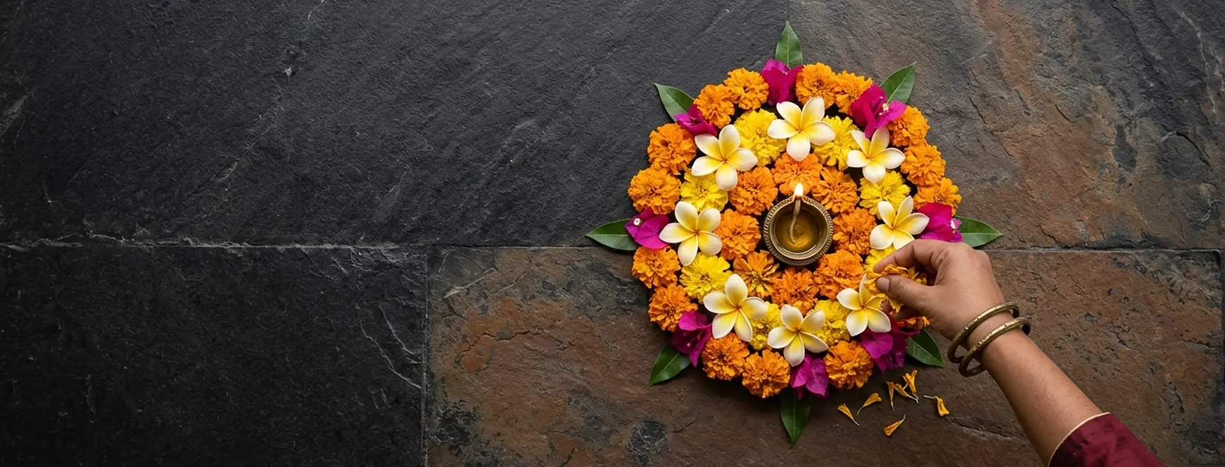A hand finishing a marigold and frangipani rangoli around a diya promotion